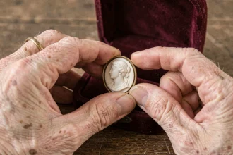 Mains de femme âgée tenant un camée ancien en coquille sculpté, posé sur un écrin en velours bordeaux, évoquant la valeur sentimentale d'un bijou transmis en héritage