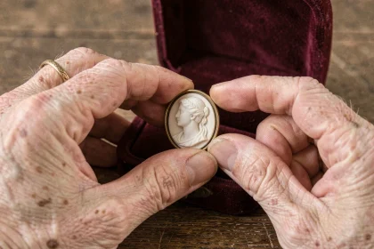 Mains de femme âgée tenant un camée ancien en coquille sculpté, posé sur un écrin en velours bordeaux, évoquant la valeur sentimentale d'un bijou transmis en héritage